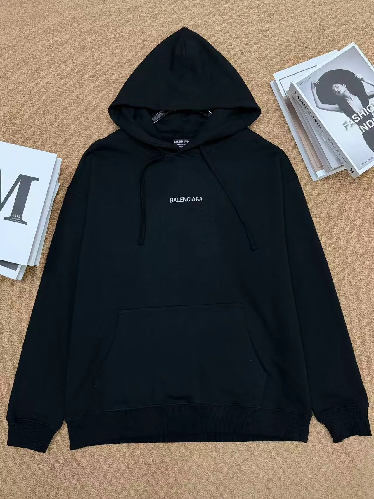 No. 2208 Style: Balenciaga Retro lettered hooded sweatshirt Color: Black, Cream White Version: Oversize loose shoulder, Same style for men and women, lazy and relaxed, covering the flesh and making you look slim Fabric: 430g high gram weight pure cotton terry fabric, soft and thick, with good drape, the upper body is not easy to wrinkle. Design highlights 1. White model: The small logo on the chest is simple and clean, minimalist and low-key style, and the daily Versatile is not picky. 2. Black model: Multi-layered Retro letter printing on the back, white rose red contrasting colors, strong layering, full of trendy atmosphere, the back printing is the visual focus of the entire dress. 3. Classic kangaroo pocket + adjustable drawstring brim, threaded cuffs and hem, Wear-Resistant is not easy to deform, and the workmanship is neatly routed. Wearing scenarios: Suitable for daily outings, commuting, and casual outings. Black is cool and stylish, and looks trendy when paired with jeans, wide-leg pants, and overalls; White is refreshing and simple, suitable for gentle casual style, and can also be worn as a couple's style. Washing and care tips: Machine wash/hand wash with cold water on the reverse side, do not rub the printed area vigorously, and dry in a cool place to avoid exposure to the sun, which may cause the print to crack and fade.